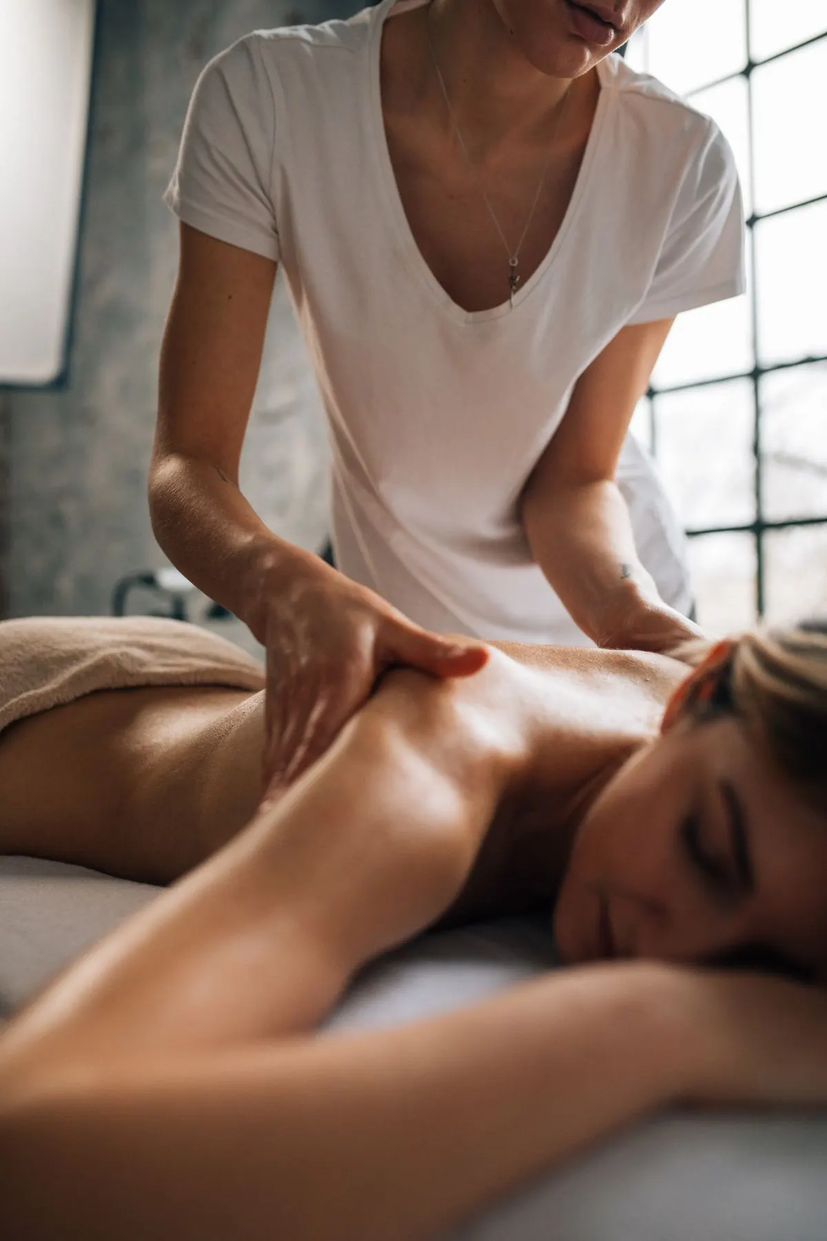 Therapist's hand resting on a seated guest's shoulder in a candlelit spa room