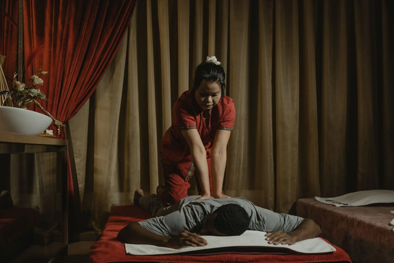 Therapist in traditional red outfit pressing a client's back on a red mat
