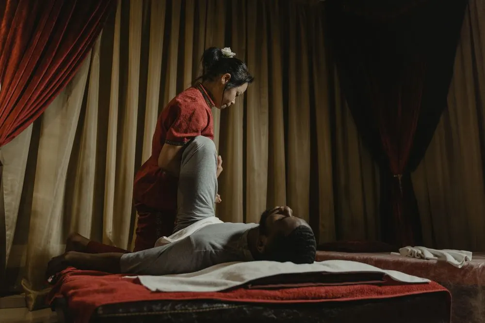 Therapist stretching a client's leg back while standing beside the mat